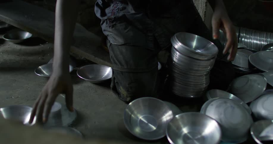 Kneeling person stacks metal bowls in concrete floored factory