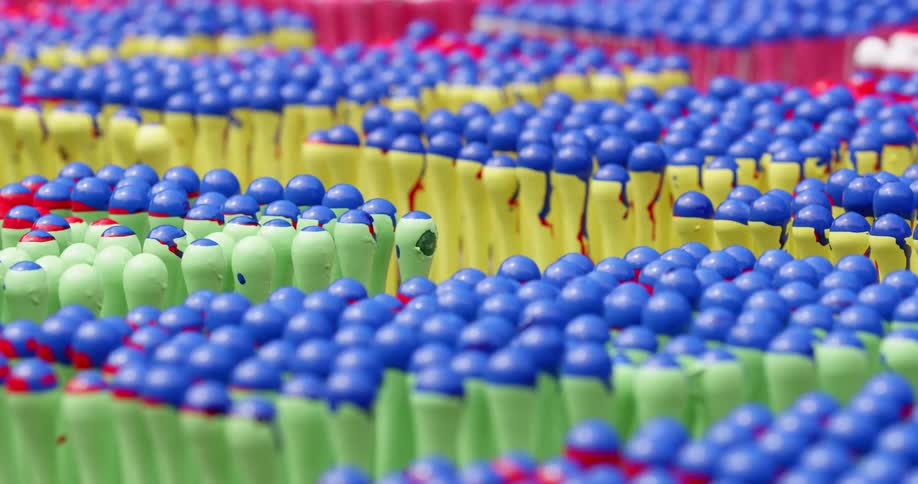 Hundreds of vertical plastic and rubber objects with a knob handle sit on trays lined up in a factory