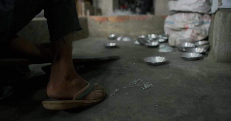 Young person wearing sandals unloads metal dishes to a recycling center in a third world country