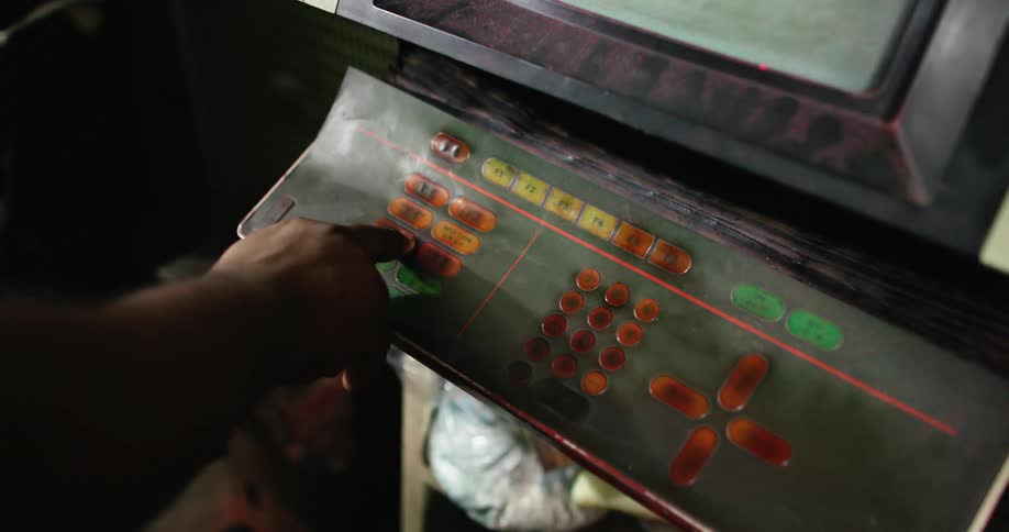 Person presses buttons on old standing game machine near store counter