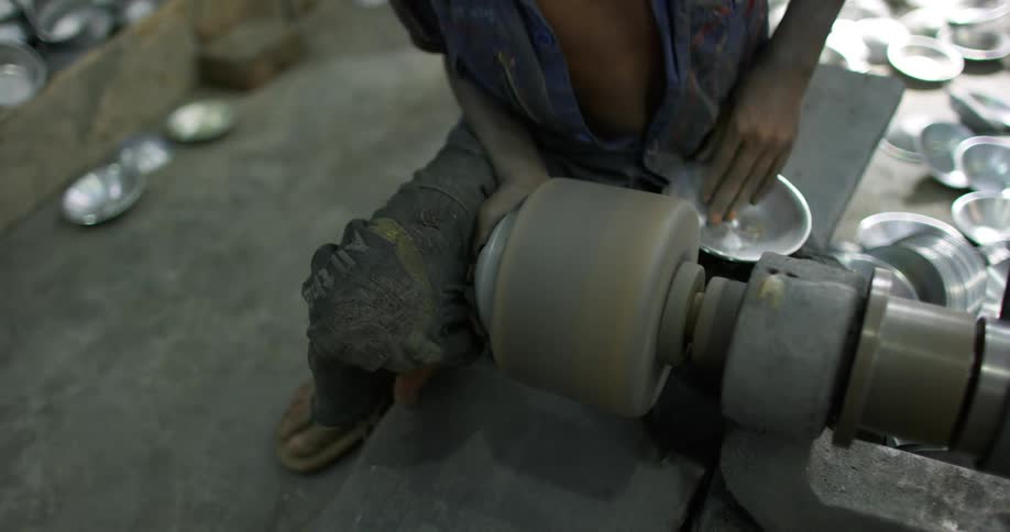 Man in dirty clothing uses large buffer to polish metal dishes