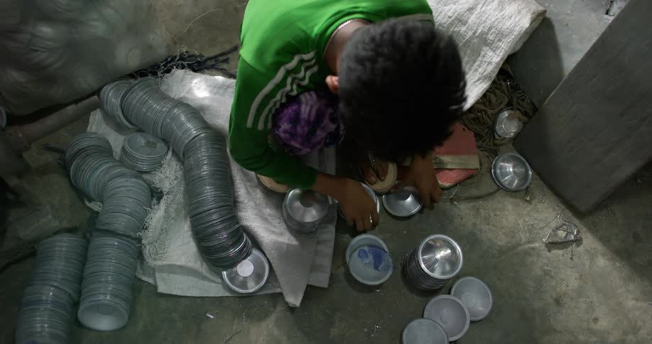 A kneeling boy quickly arranges aluminium bowls on the floor