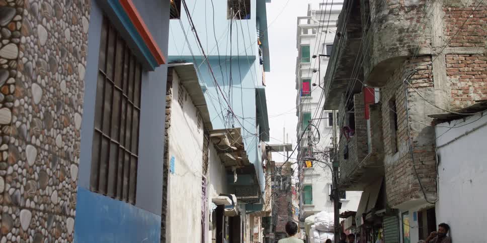 A boy walks along a narrow street between tall but old buildings during the day