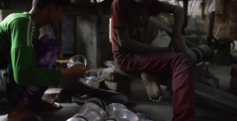 A pair of boys work in a dusty factory to produce aluminum bowls