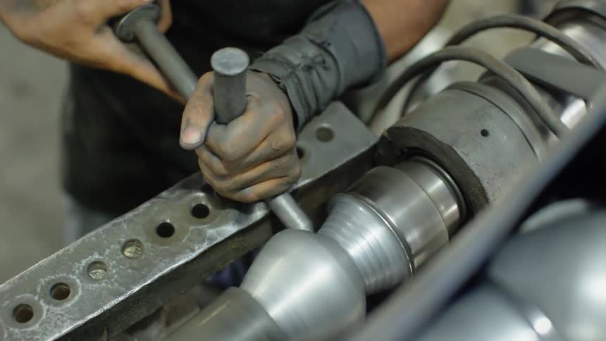 A worker uses some tools in order carve and shape a spinning piece of metal