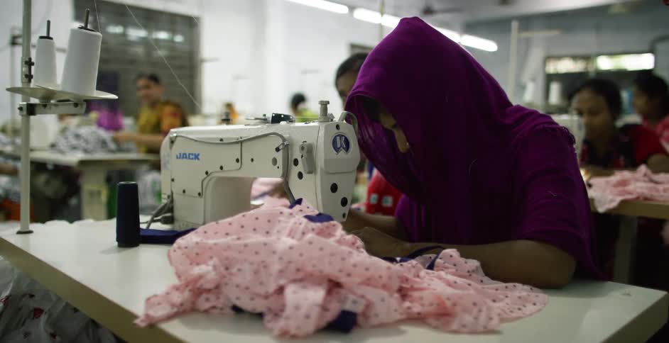 Multiple people sit at sewing machines in a sweatshop