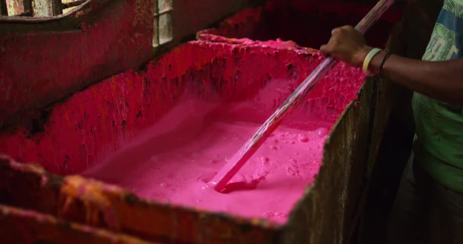 A boy stirs pink dye for balloons in large square bin near window