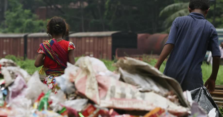 Two people in an impoverished area careful navigate through a landfill as they search through the trash