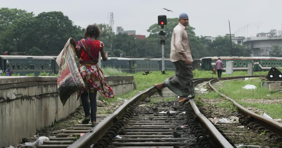 A man in a village runs across train tracks as a girl and another man walk alongside them