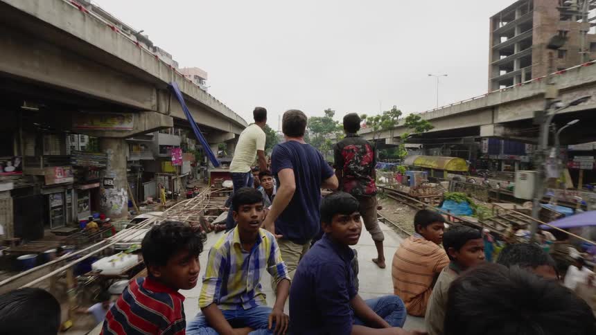 A photographer rides on a truck with a group of kids as they drive through a village and wave at crowds of people