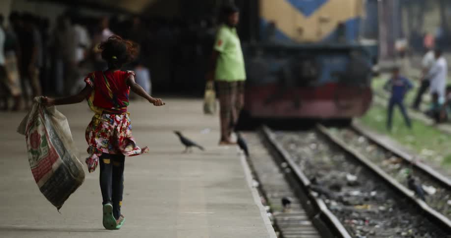 Girl carrying bag runs along train stop paralleling train tracks
