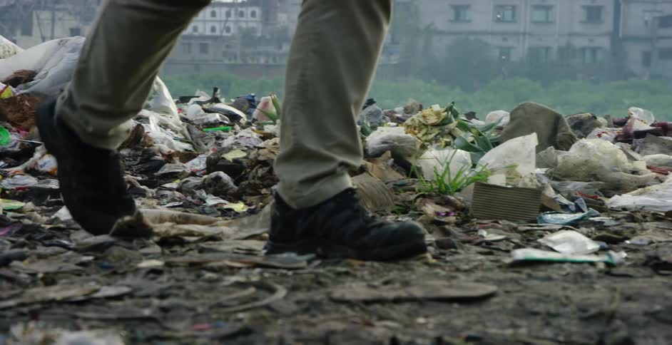 A person walks through garbage dumped in a field in a city during the day
