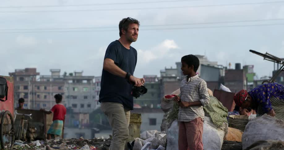 Photographer carrying a camera talks to children on a landfill in a third world country