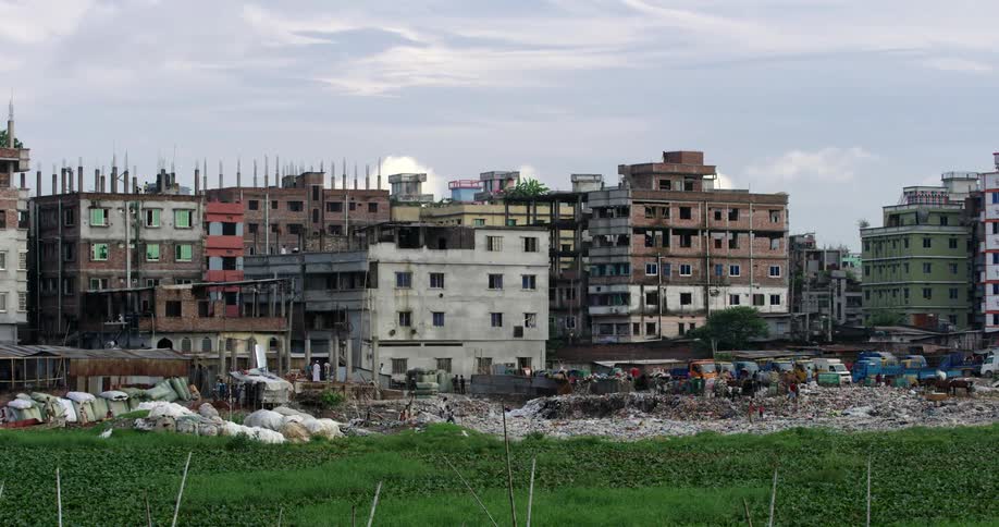People walking in piles of garbage in front of a primitive city
