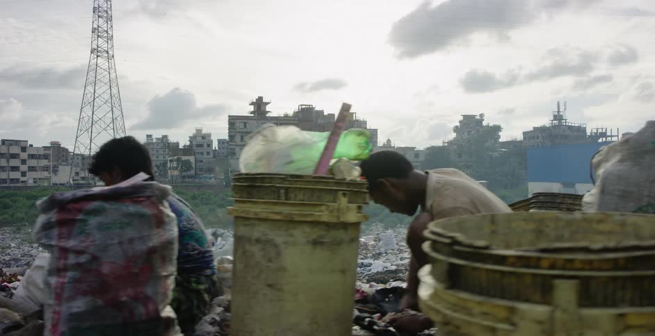 A male walking through a dump with people picking through the trash