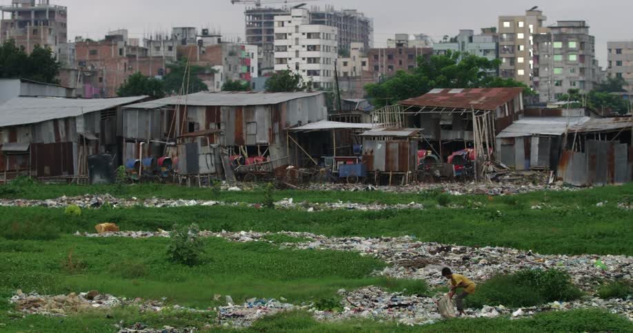 A boy picks trash from a field in a city slum during the day