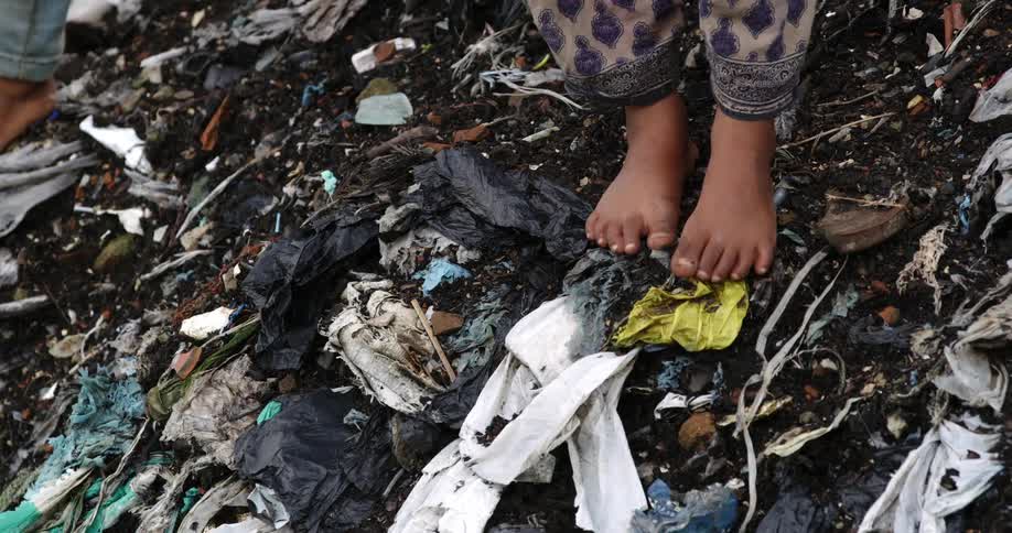 A child stands barefoot atop a mound of trash and soil
