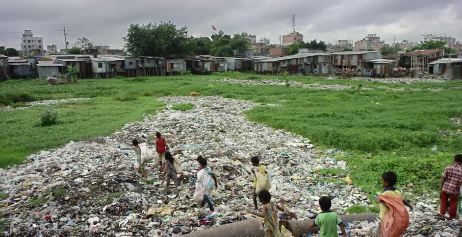Children walking through a pile of garbage and collecting items on the outskirts of a village