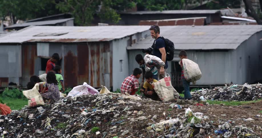 Photojournalist taking pictures of children sorting garbage in slum