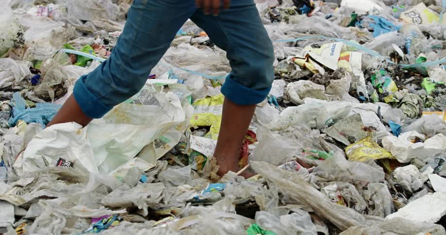 A person with jeans walking on trash barefooted