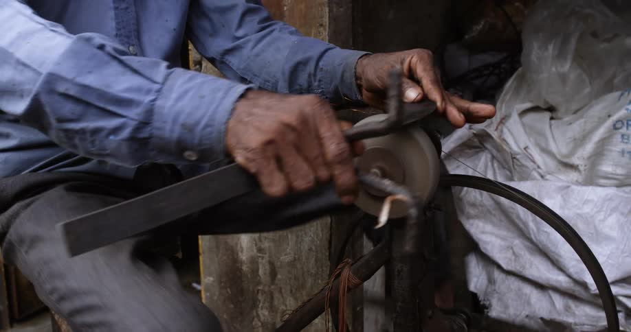 A man pedaling a spinning wheel to polish a metal piece