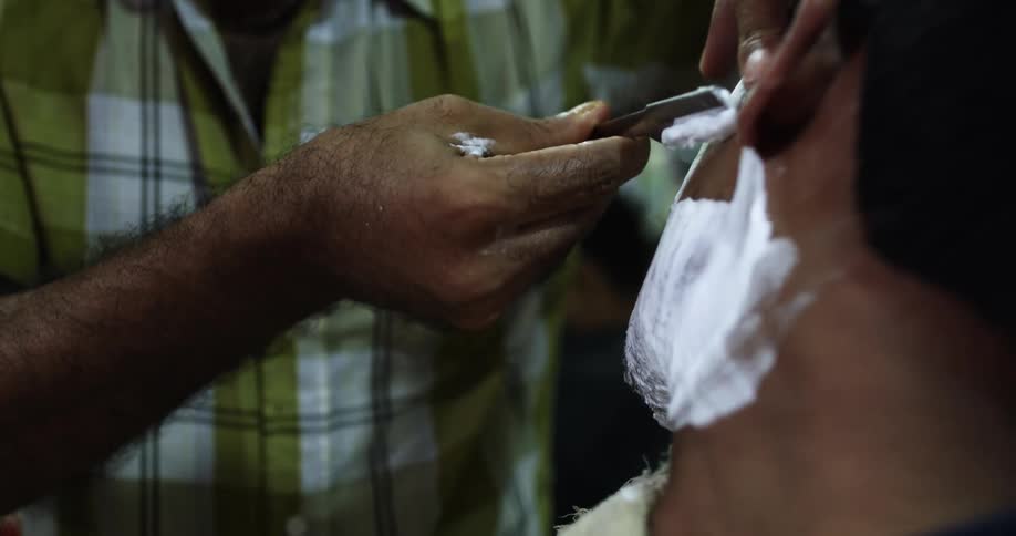 A barber uses a straight razor to shave the beard of a customer