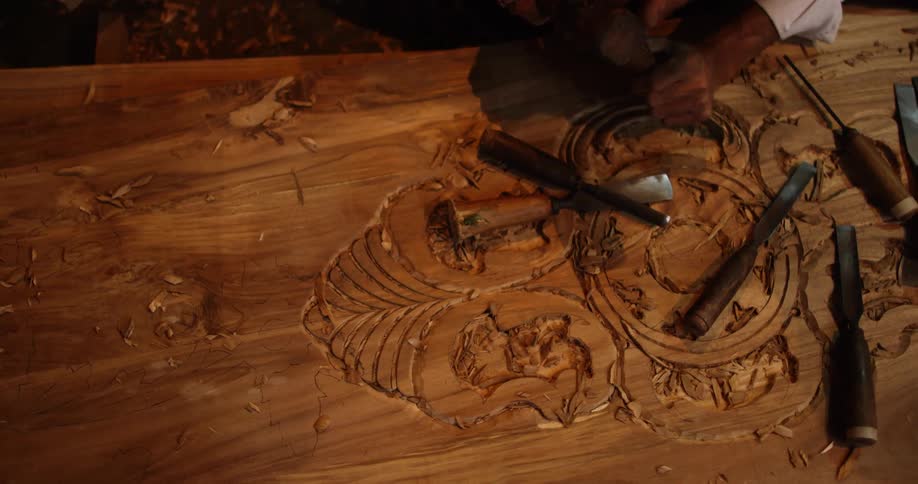 A woodcarver uses a chisel to carve artwork into a large block of wood