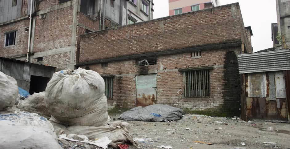 Rain falls on bags of garbage sitting outside a building in a slum