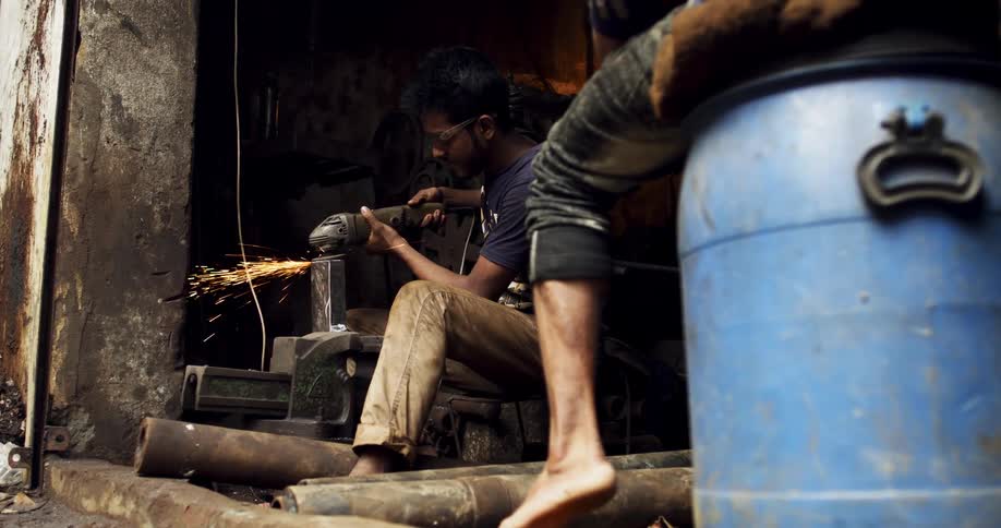 Man uses a power tool to cut metal bars on a workshop in a third world country