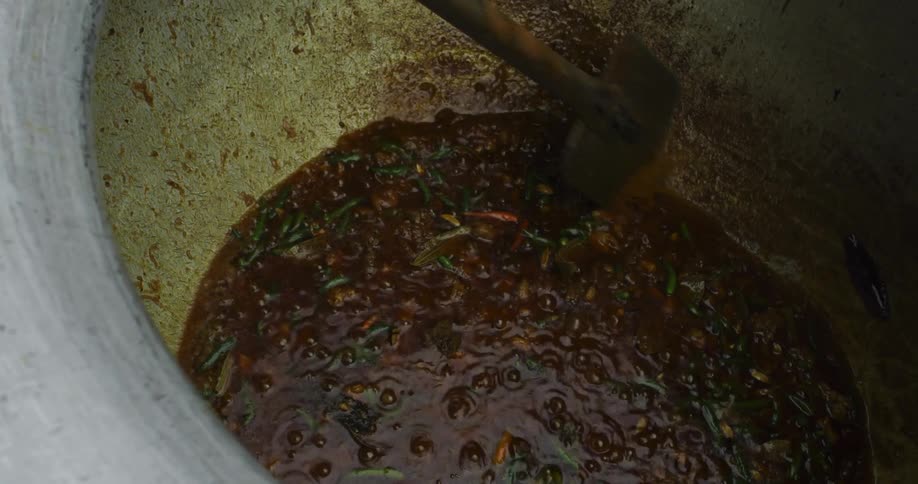 A long metal spatula is used to stir vegetables and peppers simmering in a large pot