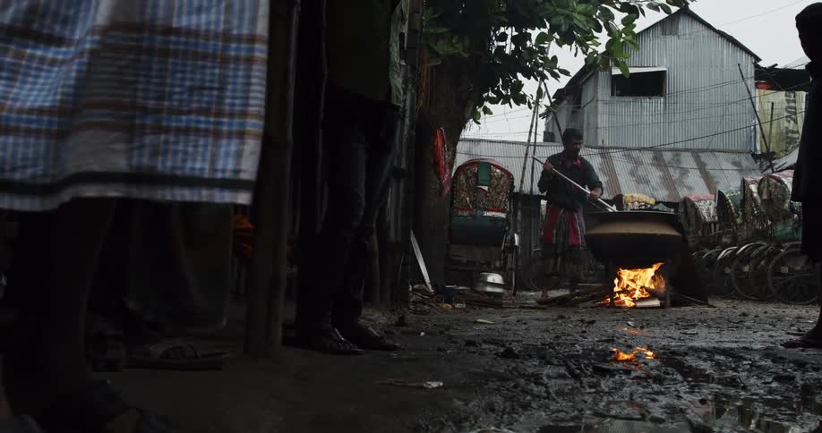 Man stirring large outdoor cooking pot in muddy yard
