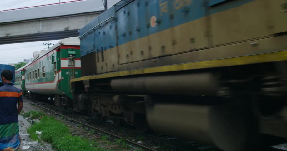 A passenger train passes through a town where pedestrian walk along the opposite track