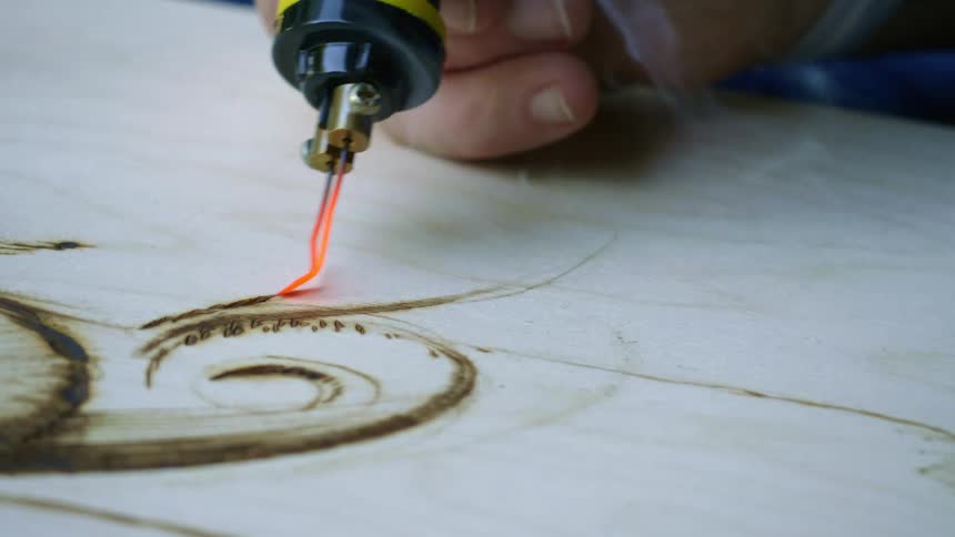 A man uses a tool to draw and burn a design onto a piece of wood