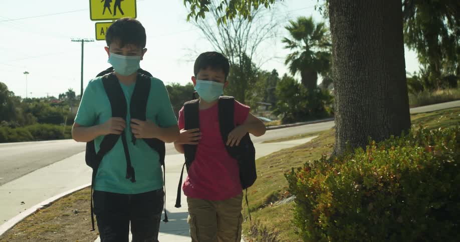 Two boys walk on a sidewalk with their backpacks wearing face masks