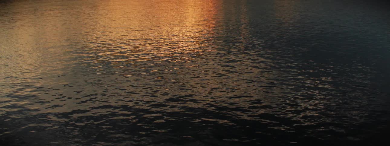 Sunset light reflecting in the surface of the dark calm waters of a lake