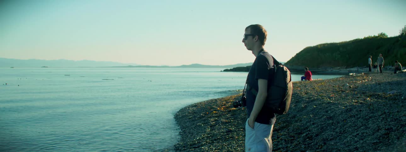 A young man stands along a rocky shoreline looking at the ocean water