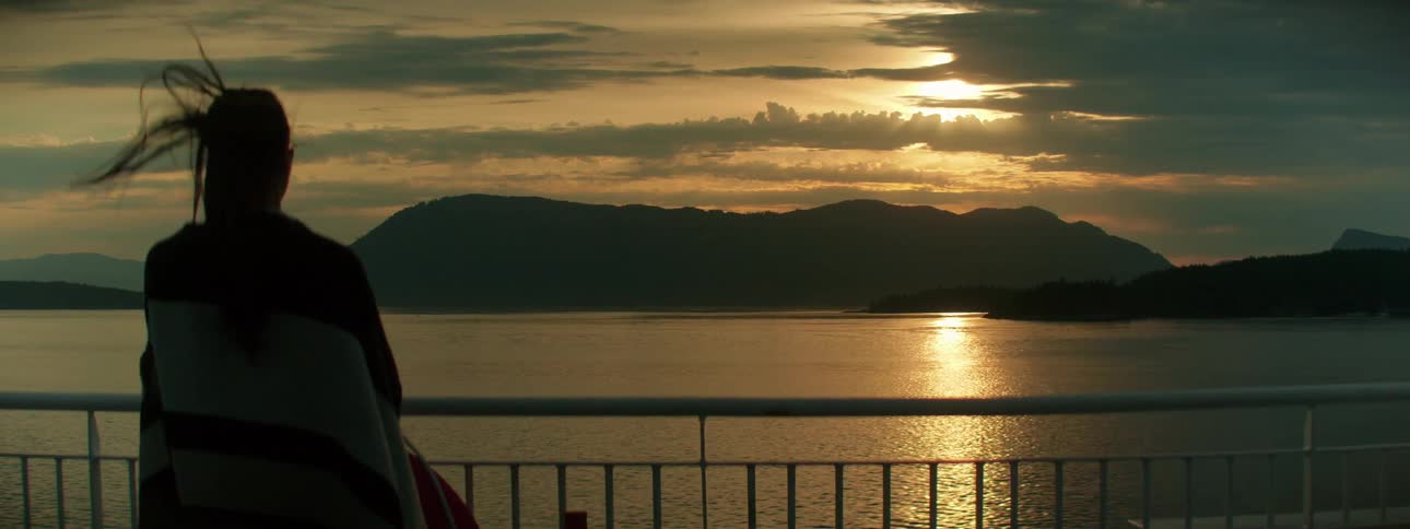 A woman stands by a railing on a boat and looks out at the water