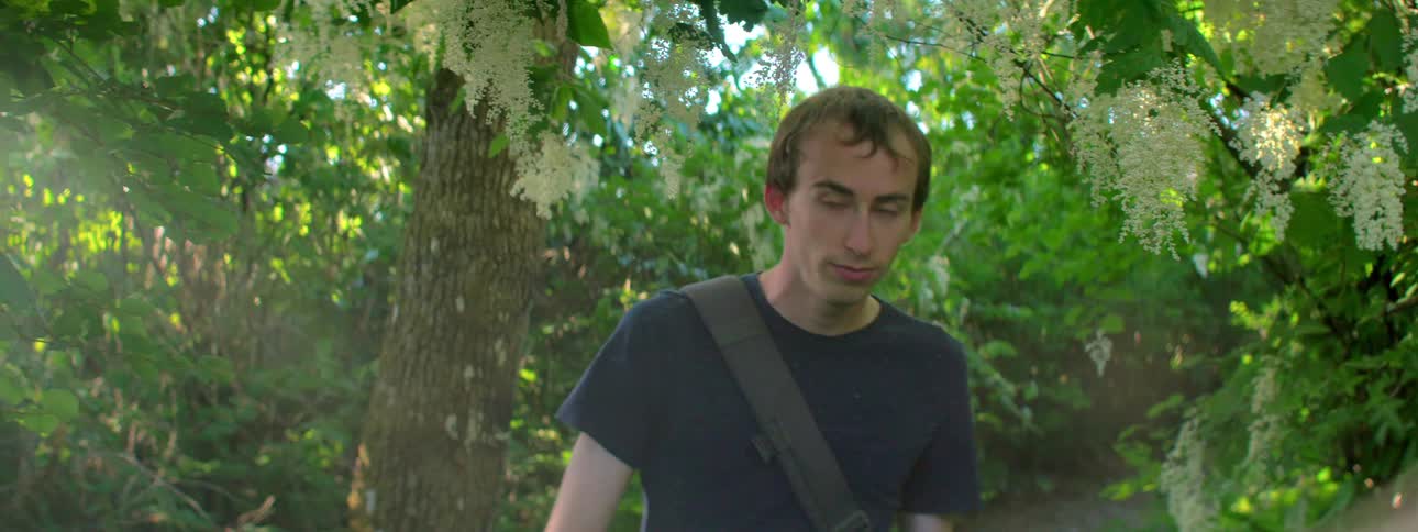 Man with a black t shirt and backpack walks on a trail under trees in the forest