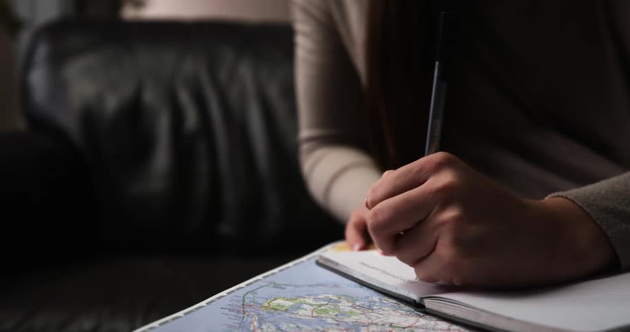 A woman sitting on a couch writing on a notebook with a pen