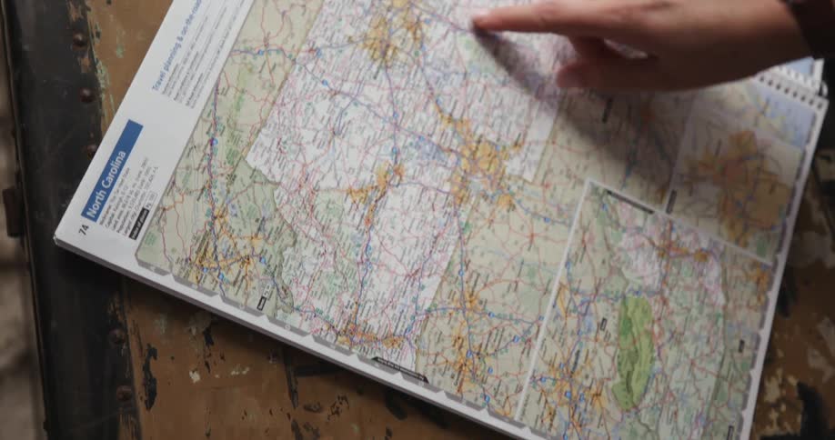 A person opens a book of maps and runs their finger along a page