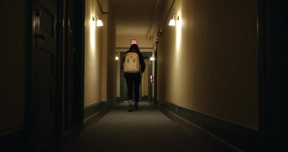 A teenage girl closes and locks the door to an apartment and walks down the hallway