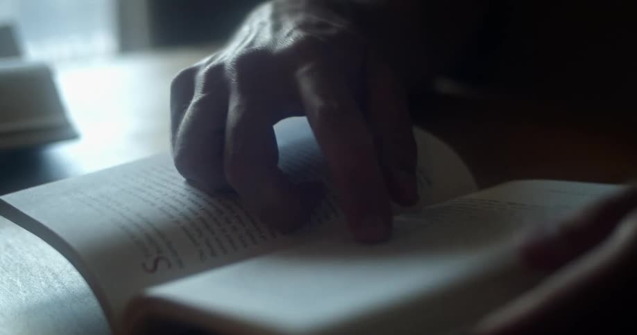 A person reading a book while sitting at a wood table