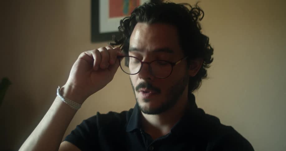 Man with a beard and a black polo shirt takes off the glasses and puts them on the table