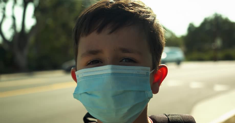 Portrait of a child standing by a neighborhood street wearing a medical face mask during the day