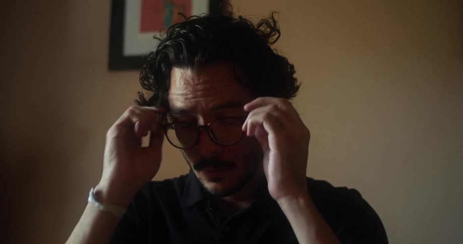 A man takes a pair of glasses off of a tabletop and puts them on his face