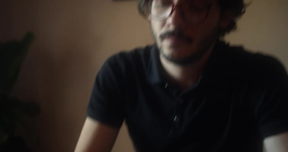Young man wearing glasses reads a book sitting in a table at home
