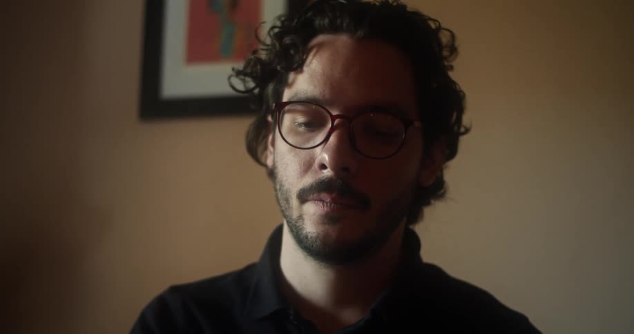 Man with a beard and a black polo shirt sits at a table and puts on glasses