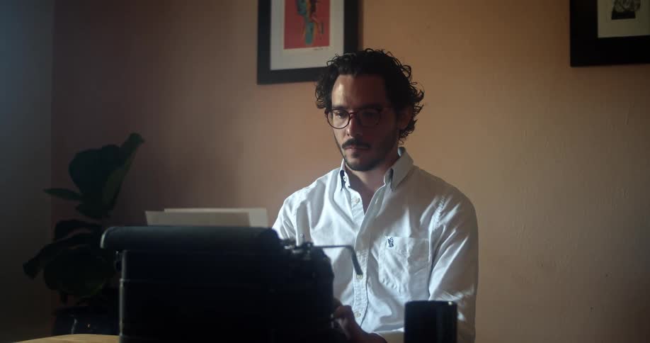 Young man wearing white shirt and glasses writes on a typewriter in a room