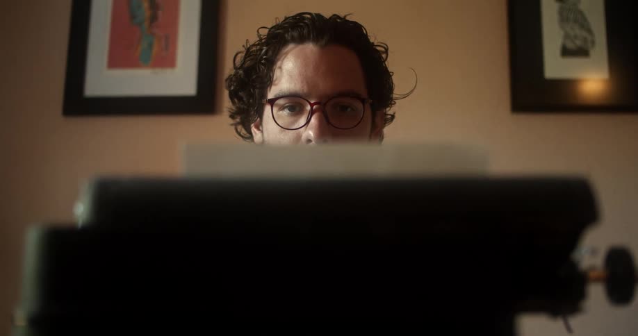 A man is typing on a mechanical typewriter in a home office during the day