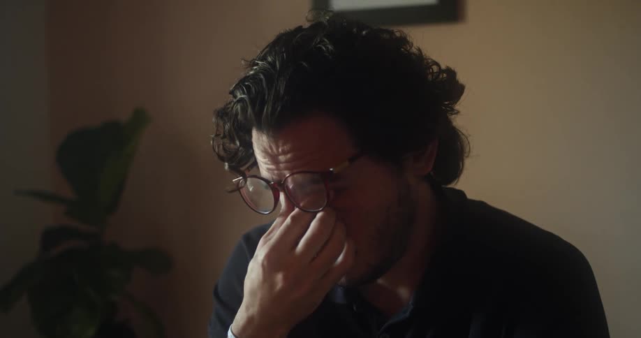 A man is sitting in a room and wearing glasses